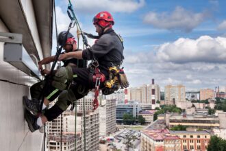 Industrial mountaineering worker hangs over residential building while installing and repairing equipment. Rope access laborer hangs on wall of house. Concept of high-rise urban works. Copy space