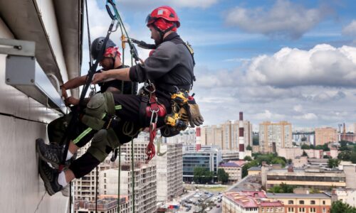Industrial mountaineering worker hangs over residential building while installing and repairing equipment. Rope access laborer hangs on wall of house. Concept of high-rise urban works. Copy space
