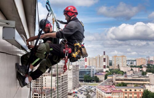 Industrial mountaineering worker hangs over residential building while installing and repairing equipment. Rope access laborer hangs on wall of house. Concept of high-rise urban works. Copy space