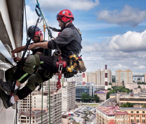 Industrial mountaineering worker hangs over residential building while installing and repairing equipment. Rope access laborer hangs on wall of house. Concept of high-rise urban works. Copy space